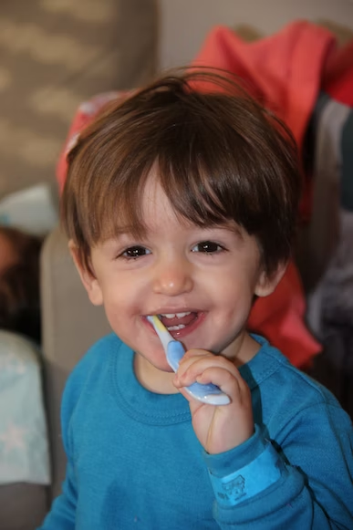 a little boy smiling while brushing his teeth
