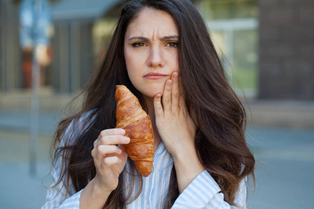 a woman holding a croissant and her jaw on the other hand  while frowning in pain