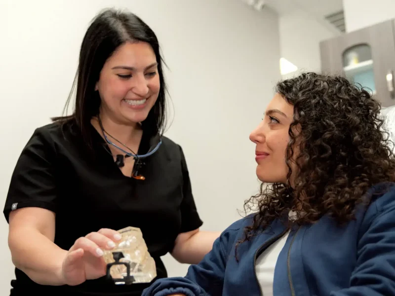 Dental professional explains procedure to patient using jaw model.